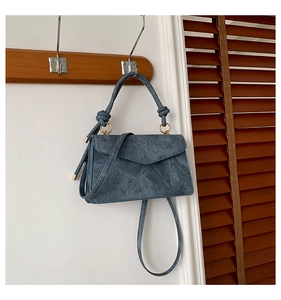 Dettaglio borsa a mano blu in denim con manico a nodo decorativo e finiture metalliche dorate