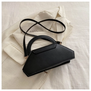 Detail of a black geometric leather handbag on a white blazer showing handle and strap