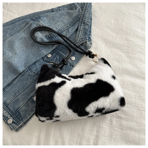 Detailed view of plush cow print hobo bag with black leather strap on denim fabric