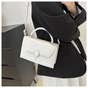 Vue détaillée du sac à main blanc avec accents dorés porté sur un blazer noir