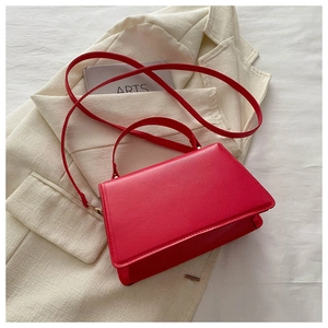 Top view of vibrant red crossbody handbag placed on a minimalist ivory white blazer