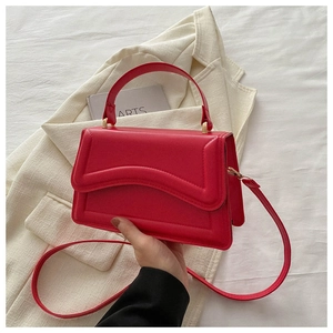 Close-up of a red leather handbag with wave-shaped flap and gold metal hardware