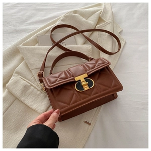 Detailed close-up of dark brown quilted crossbody bag on cream blazer with gold metal lock