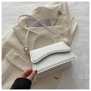 Close-up of white leather handbag with gold hardware on a textured blazer background