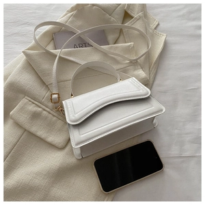 Detailed view of white structured handbag with gold hardware on a beige blazer