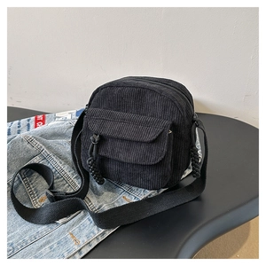 Detail of a black corduroy crossbody bag with front flap pocket and zipper closure