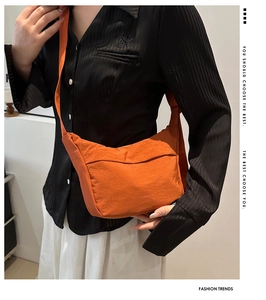 Detail view of an orange nylon crescent crossbody bag worn over a black striped shirt