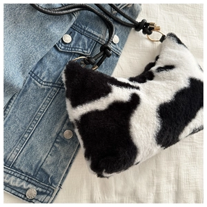 Close-up of plush cow print shoulder bag with black strap and golden metal ring detail