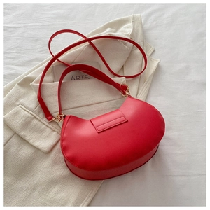 Detailed shot of bright red crescent bag with golden buckles on a beige blazer background