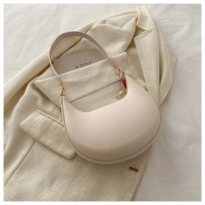 Detail of a creamy white half-moon underarm bag with gold hardware on a textured blazer