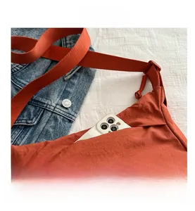 Detail showing an orange tote bag front pocket holding a smartphone on a denim jacket