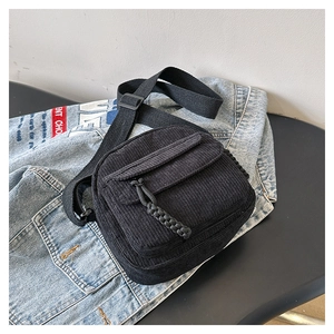 Detail of black corduroy crossbody bag featuring a woven zipper pull on denim background