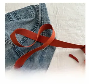 Detail of adjustable orange nylon shoulder strap with metal buckle on denim background
