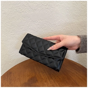 Detailed view of quilted leather texture on a black envelope clutch held by a model