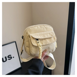 Detail of cream corduroy shoulder bag showing texture, front flap pocket and woven puller