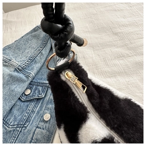 Detail of plush black and white shoulder bag with golden zipper and knotted leather strap
