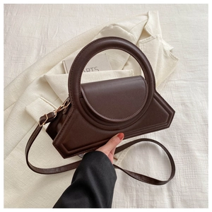 Detail of deep brown geometric crossbody bag with a round handle and gold hardware