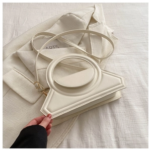 Detail of white geometric handbag with circular hollow handle on a white fabric background