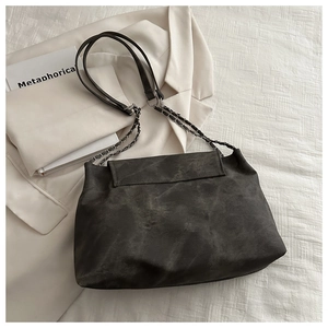 Detail of dark grey crossbody bag with silver chain strap on a white blazer background