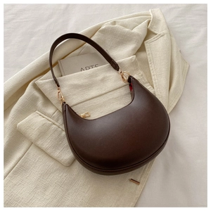 Detailed view of brown crescent shoulder bag with gold hardware on a cream blazer