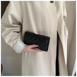 Close-up of elegant black quilted leather clutch bag held by a model in a beige coat