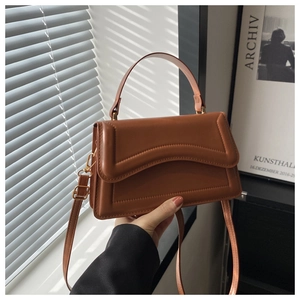 Detail of caramel faux leather handbag with wave flap and gold-tone metal hardware