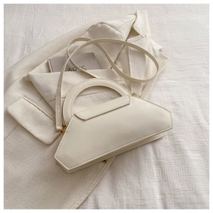 Detail of cream white trapezoid handbag with gold hardware on white textured fabric