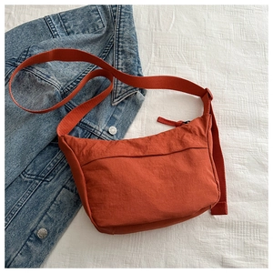 Macro detail of brick red nylon crossbody bag with adjustable strap on denim background