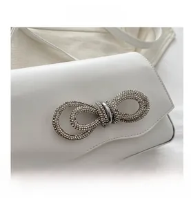 Close-up of a white leather crossbody bag featuring a sparkling rhinestone bow buckle