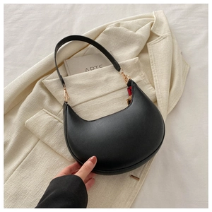 Close-up of black PU leather crescent underarm bag with gold zipper on beige blazer