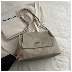 Close-up of beige tote bag with matte texture, metal chain strap and logo plaque