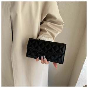 Detail of a black quilted leather clutch bag held by a model in a beige coat