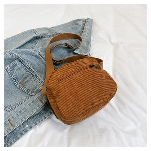 Detail view of brown corduroy crossbody bag with zipper pocket on textured white fabric