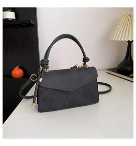 Detail of dark grey flap bag featuring decorative knotted handle and gold-tone hardware