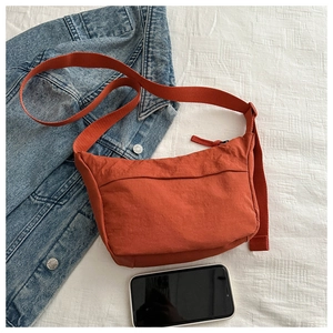 Flat lay of an orange messenger bag with wide shoulder strap on white fabric background