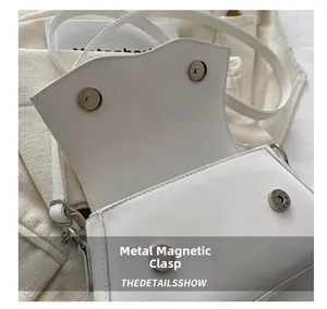 Detail view of the silver magnetic snap closure on the white leather crossbody flap bag
