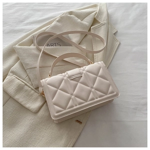 Detailed view of quilted beige handbag featuring gold hardware on a cream blazer