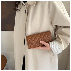 Close-up of brown quilted leather clutch bag held against a beige trench coat
