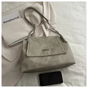 Detail view of MIKXAIQI metal logo and grey-green soft faux leather texture on tote bag
