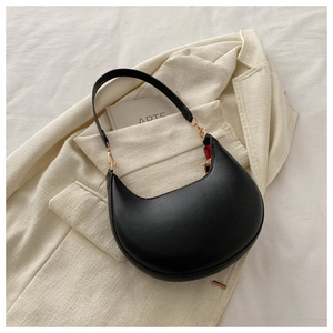 Detail of black semi-circle shoulder bag with gold hardware on a beige blazer background