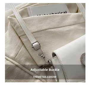 Detail of silver metal buckle and strap on white PU leather handbag with rhinestones