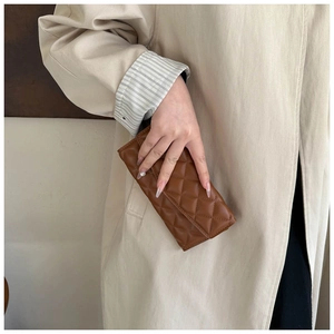 Close-up of brown quilted leather clutch with silver hardware clasp held by a model