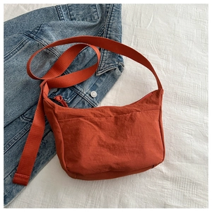 Detail of a bright orange nylon crossbody bag on white fabric with denim jacket