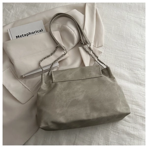 Detail of grey-green suede chain bag with silver strap on white blazer background