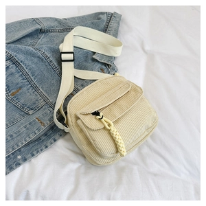 Detail of beige corduroy shoulder bag with white strap and yellow charm on denim jacket