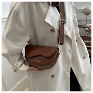 Gros plan d'un sac demi-lune marron foncé avec rabat ondulé et bandoulière large