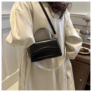 Detail of elegant black leather handbag held by model in casual French style setting