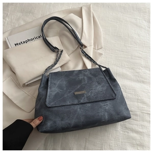 Detail of grey denim tote bag showing metal plaque and chain strap on white blazer
