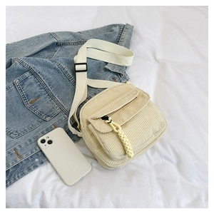 Detail view of cream corduroy shoulder bag with front flap pocket and yellow zipper pull