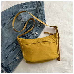 Detail of ginger yellow nylon crossbody bag with strap on blue denim background